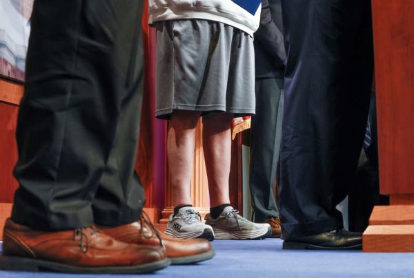 Fetterman's lower half in sweatshirt and gym shorts standing next to men in suits.