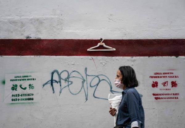 A woman walks past graffiti made by feminist organizations announcing telephone lines and social networks to help women who want an abortion in Caracas on July 14, 2023. Photo by Magda Gibelli/AFP