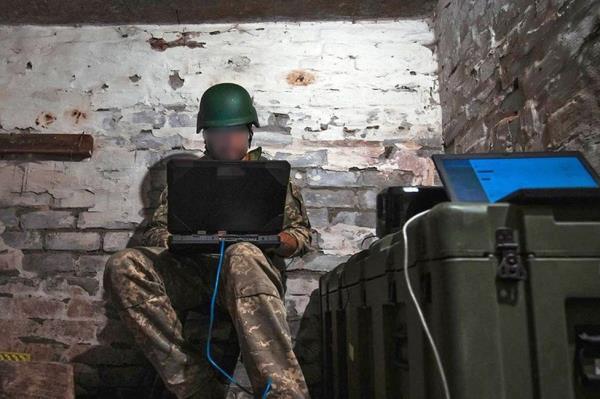 Ukrainian soldier leans over his laptop in a damp ba<em></em>sement