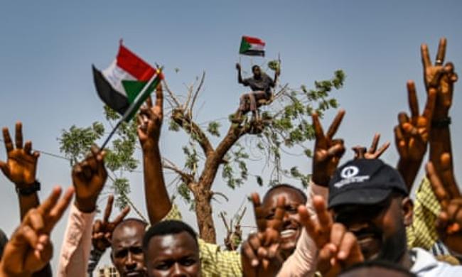 TOPSHOT-SUDAN-POLITICS-UNREST-DEMOTOPSHOT - Sudanese protestors chant slogans and flash victory signs as another waves a natio<em></em>nal flag from atop a tree behind, during a protest outside the army complex in the capital Khartoum on April 17, 2019. - Sudanese protesters hardened their demand that the military men in power quickly step down and make way for civilian rule, refusing to budge from their sit-in outside army headquarters. (Photo by OZAN KOSE / AFP)OZAN KOSE/AFP/Getty Images