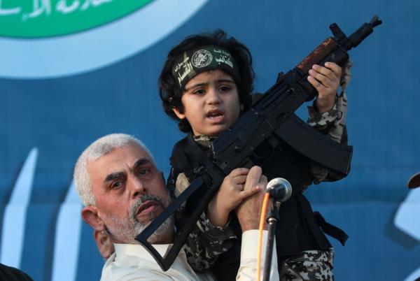 Sinwar holds a child in a soldier costume, on stage with a weapon for the cameras, at a rally of supporters in 2021.