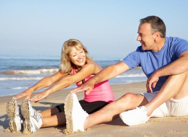 senior couple stretching on the beach, co<em></em>ncept of healthy lifestyle habits that are prematurely aging you