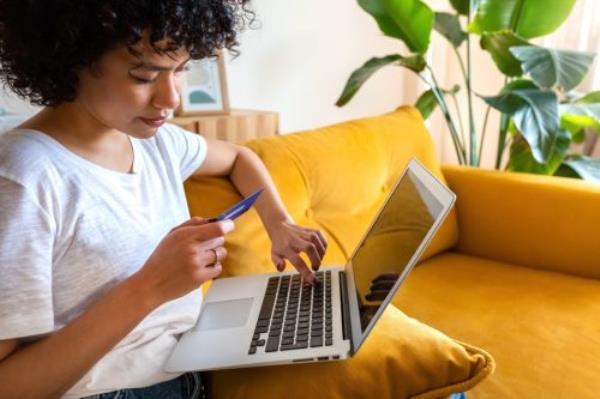 Close up of woman sitting on the couch using credit card and laptop to shop o<em></em>nline from home. 