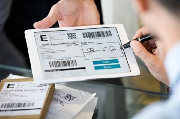 Close up hand of businessman signing on digital tablet while receiving parcel. Man signing delivery service docu<em></em>ment on tablet after receiving package. Signing digital docu<em></em>ment after receiving parcel from courier in office.