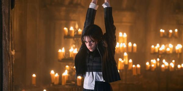 Jenna Ortega hanging in chains as Wednesday with candles behind her.