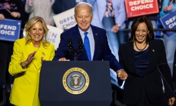 White woman in yellow suit, white man in navy suit, Black woman in black skirt suit on stage, all smiling brightly.