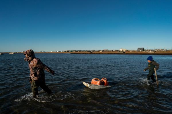 Pulling a sled with fuel co<em></em>ntainers in the lagoon, Joe Eningowuk, 62, left, and his 7-year-old grandson, Isaiah Kakoona, head toward their boat through the shallow water while getting ready for a two-day camping trip in Shishmaref, Alaska, Oct. 1, 2022. 