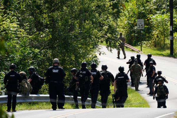 Police are seen walking down a winding road lined with thick brush as they searched for Cavalcante.