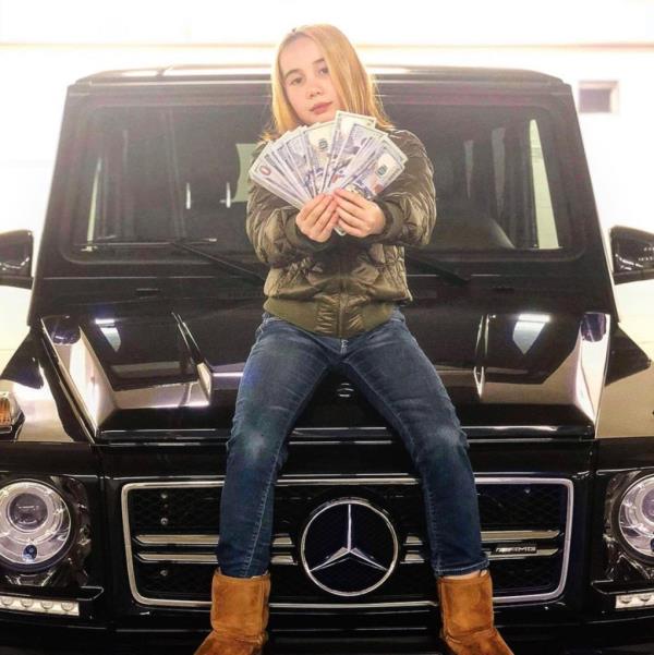 Lil Tay sitting on a Mercedes SUV and holding stacks of cash