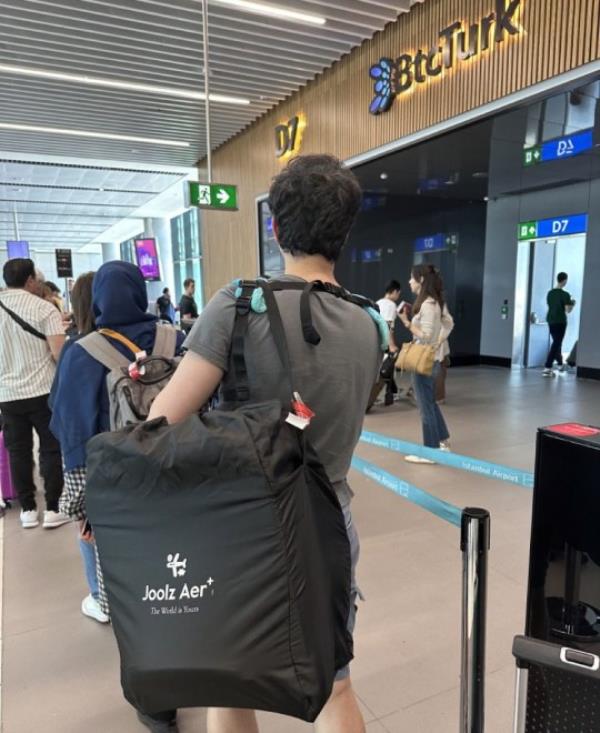 Man standing at airport gate carrying Joolz Aer+ pushchair on his shoulder in its travel bag