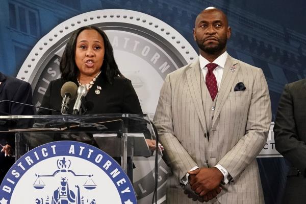 Fani Willis speaks into a microphone at a press co<em></em>nference with Nathan Wade standing by her side.