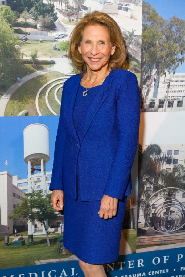 Shari Redstone standing and smiling wearing a purple suit.