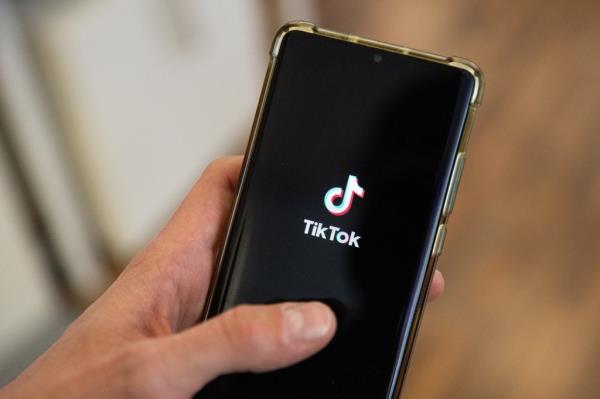 A man holding a smartphone displaying the logo of social media platform Tiktok.