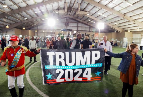 Two people holding a Trump flag - Thien Tran from San Diego and Quinn Foley from Las Vegas - wait for Do<em></em>nald Trump to speak at a campaign rally.