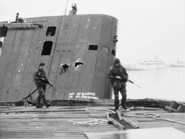 A 1982 photograph of two Royal Marines patrolling past the damaged fin of the abando<em></em>ned Argentine submarine Santa Fe, on which the shooting took place