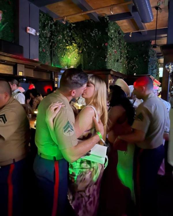 A man and woman kissing at the Single and The City fleet week party in NYC, surrounded by firemen in uniform