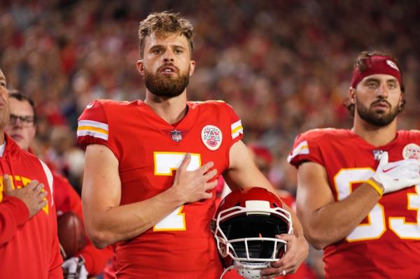 Harrison Butker, in Chiefs uniform and holding his helmet in one hand with his other hand over his heart