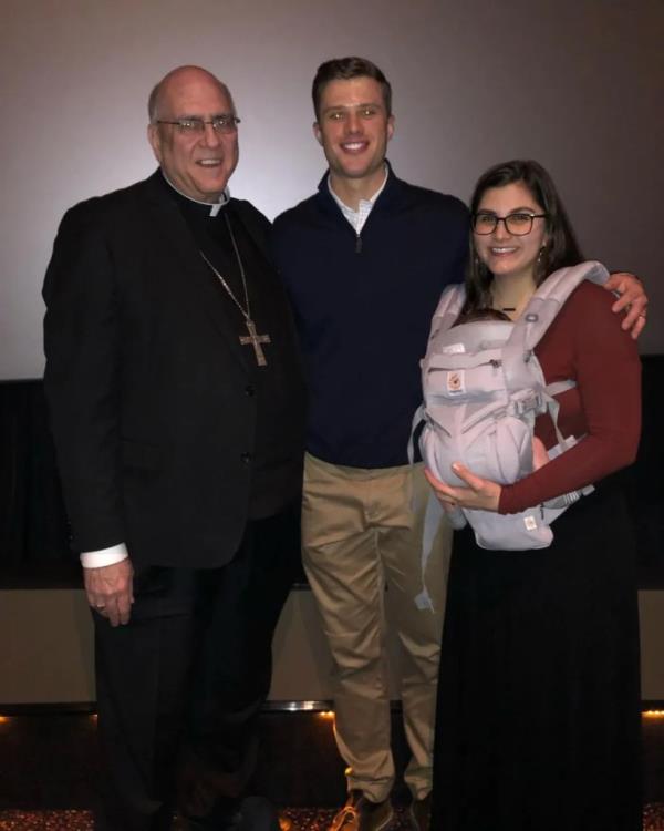 Harrison Butker poses with his wife Isabelle and a priest.