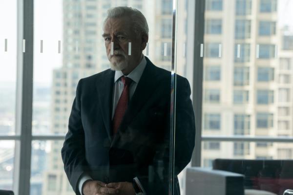 Brian Cox standing in an office looking serious. 