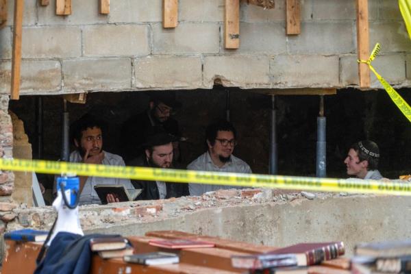 Hasidic Jewish students sit behind a breach in the wall of a synagogue that led to a tunnel dug by the students.