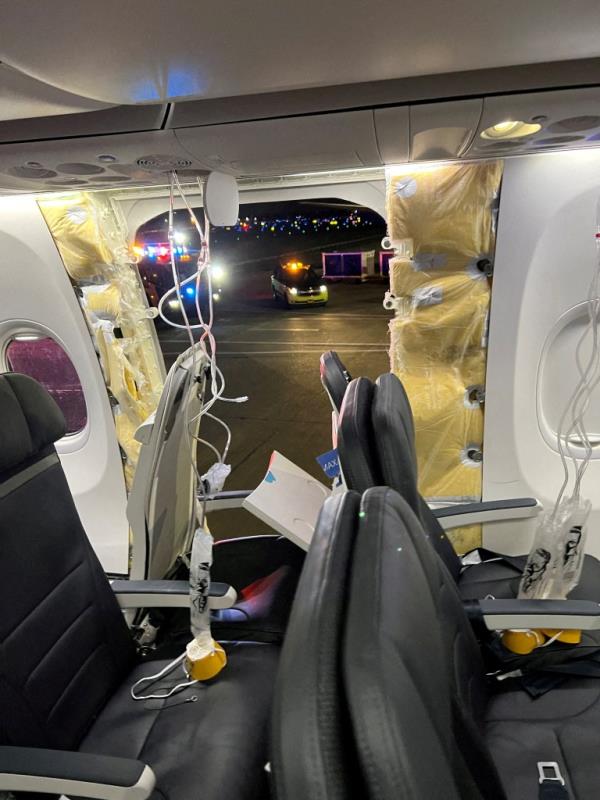 Passenger oxygen masks hang from the roof next to a missing window and a portion of a side wall of an Alaska Airlines Flight 1282