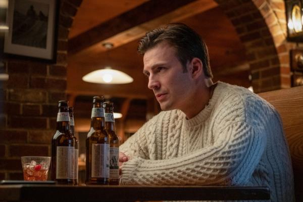 Chris Evans in his famous white sweater, glowering, in a booth. 