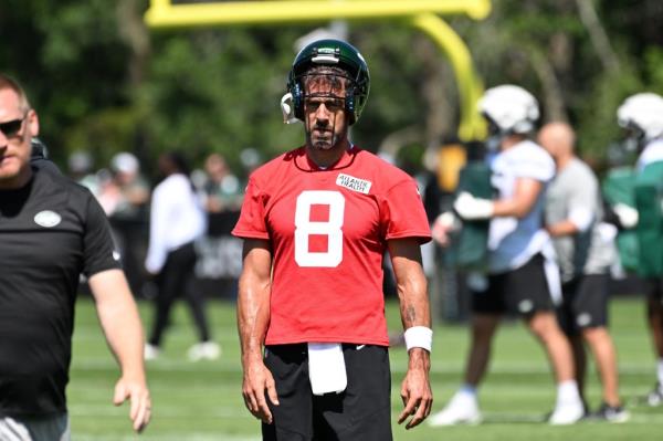 rodgers on the field at practice in a red jersey with white letters and black shorts and his helmet halfway on his head