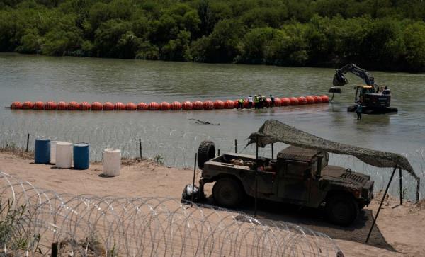 Workers assemble large buoys to be used as a border barrier