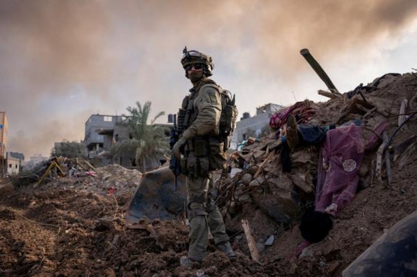 An Israeli soldier standing amid smoke and rubble in the Gaza Strip