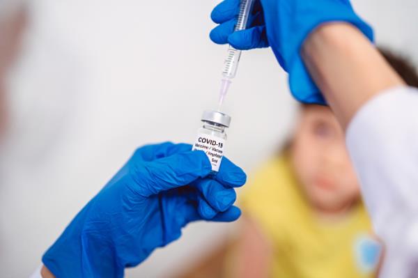 Medical doctor in protective gloves filling injection syringe with COVID-19 vaccine and ready to give kid girl Covid-19 vaccination