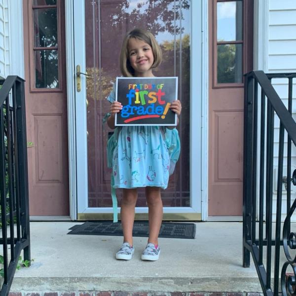 A little girl standing on her front stoop holding a sign that says 