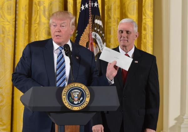 US President Do<em></em>nald Trump holds the letter left for him by former US President Barack Obama, as Vice President Mike Pence watches, before the swearing in of the White House senior staff at the White House on January 22, 2017, in Washington, DC.