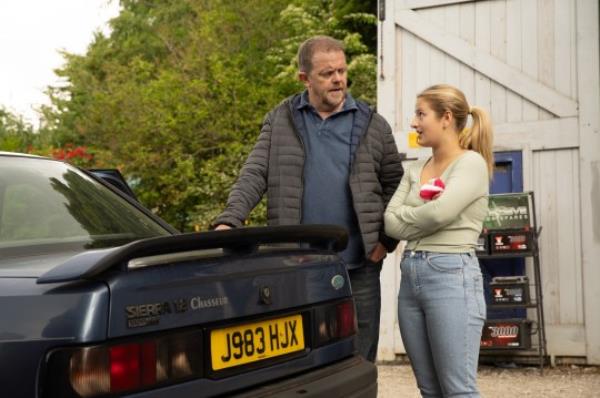 Dan and Amelia are outside the garage debating whether or not to leave the Emmerdale village