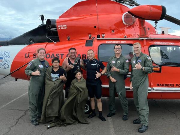 A man and his two sons smile at the camera along with the helicopter crew and rescue swimmer who saved them from their capsized boat.