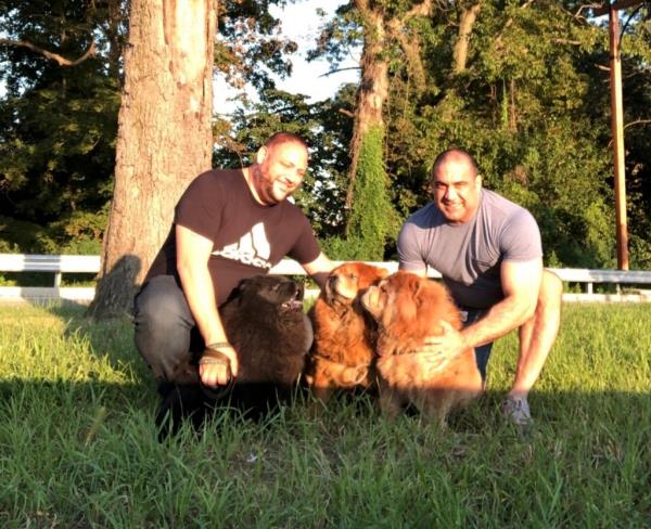 Anthony Russo and Miguel Manzi standing in a grassy area with their dogs