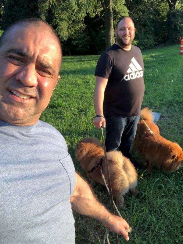 Anthony Russo and Miguel Manzi posing for a selfie with their dogs in the park