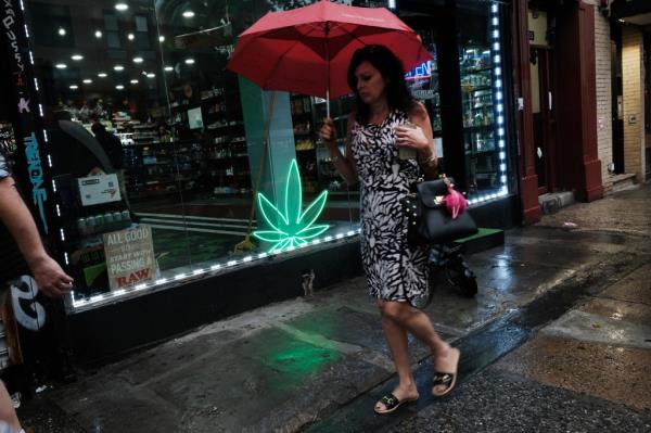 A woman walking past a smoke shop with a marijuana leaf display in the window in New York City