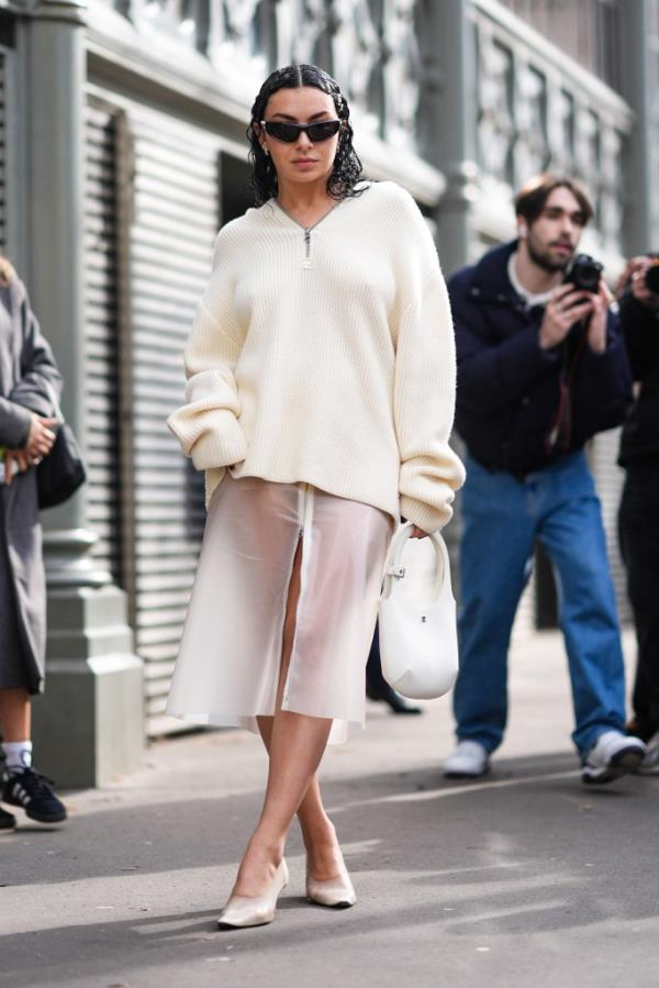 Charli XCX wearing a white wool pullover, a midi skirt with transparent details, high heels and black sunglasses at Paris Fashion Week Fall/Winter 2024/2025