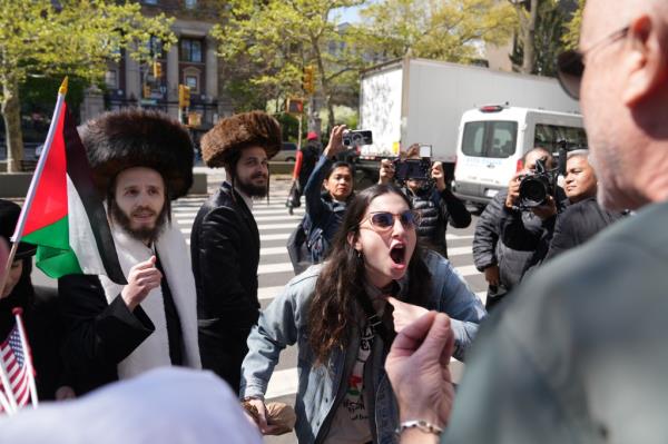 A woman screams at someone, while two Orthodox men with fur hats on look on.