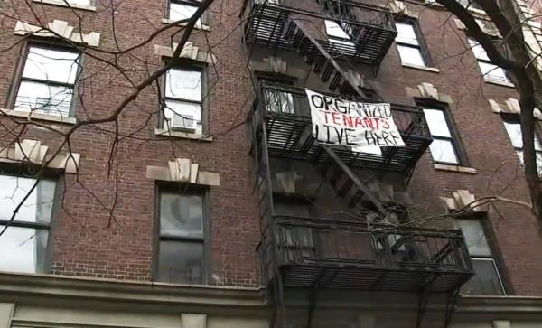 A sign hangs from an apartment. 