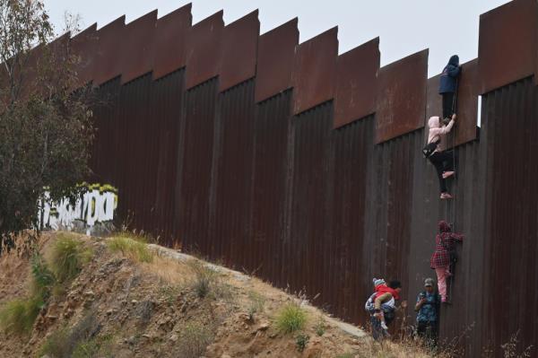 A group of adult and child migrants climbing the border wall between Tijuana and San Diego seeking asylum in the United States