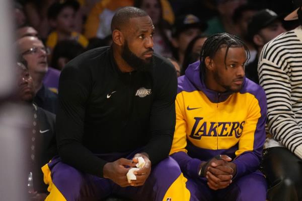 LeBron James and Bro<em></em>nny James sitting alo<em></em>ngside each other on the bench.