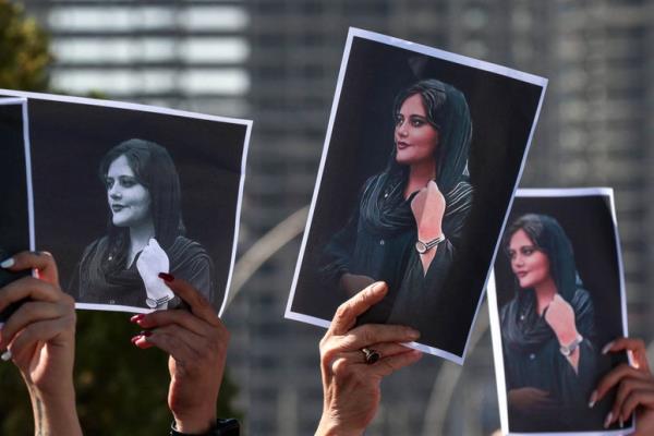 Close-up view of protestors' hands holding up pictures of Mahsa Amini.